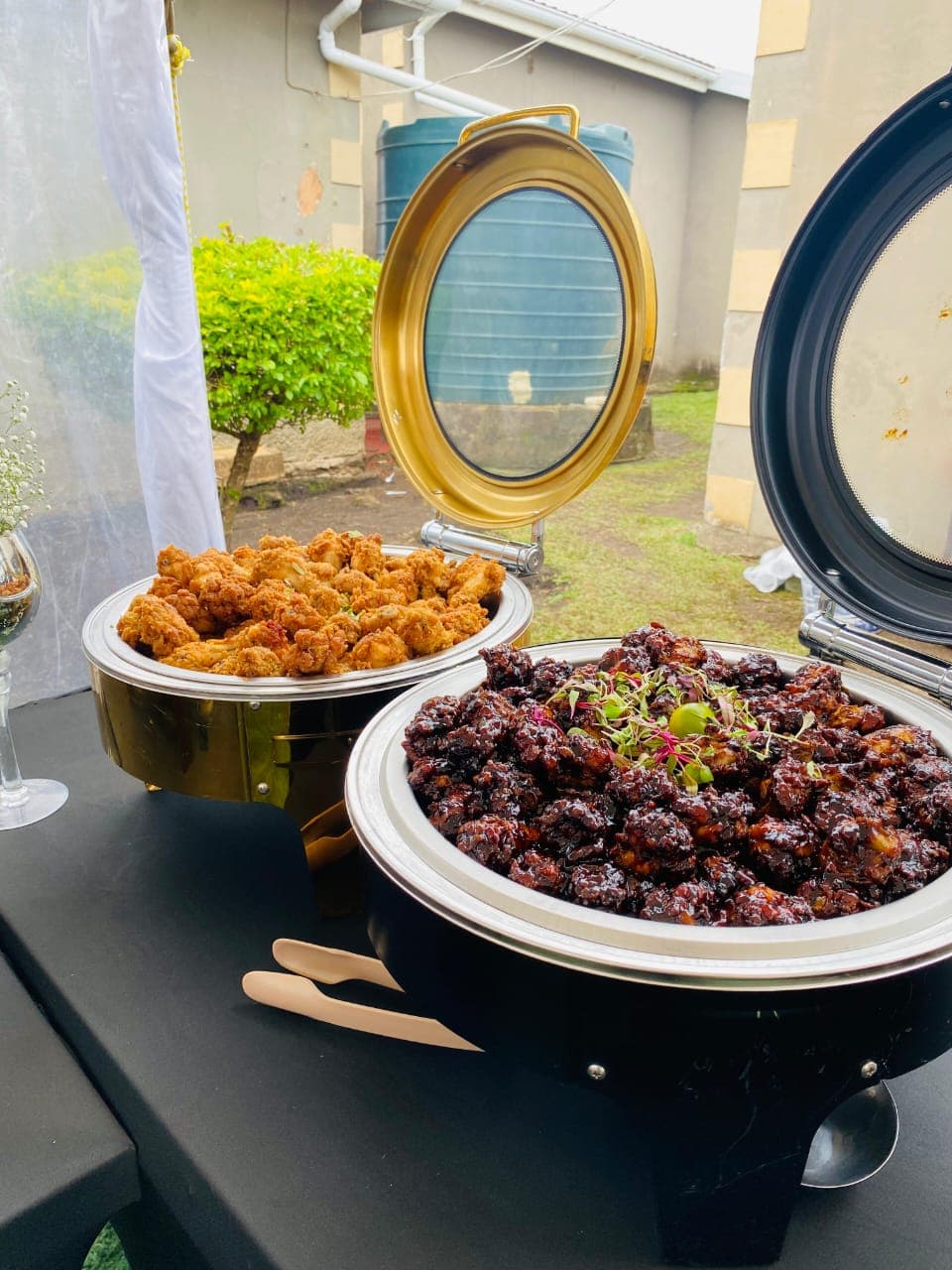 Chafing dishes of fried and glazed chicken set up at an outdoor event